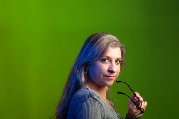 Model portrait with prescription glasses in hands against green background. She manipulates the glasses. Relaxed calm woman.