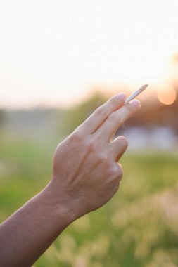 Umumi bir yerde erkek eli sigara tutuyor.