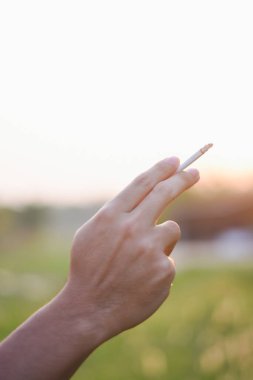 Umumi bir yerde erkek eli sigara tutuyor.