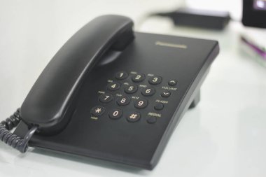 İletişim için kullanılan masanın üzerindeki siyah ofis telefonu.
