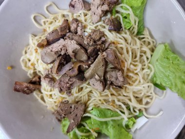 Beyaz bardakta kurutulmuş sarı şehriye, tavuk sakatatı ve birkaç sebze.