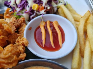 Sebzeli kızarmış tavuk bifteği ve antika ahşap masada beyaz tabakta sos. Bıçaklar ve çatal bıçak takımı var..