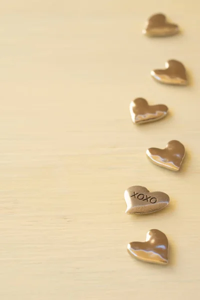 Metal hearts, one with xoxo on it, are photographed along the edge of a weathered table.