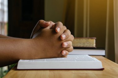 Dua eden eller ahşap masadaki kutsal İncil 'in üzerinde pencere ışığıyla. Hıristiyan arka planı.