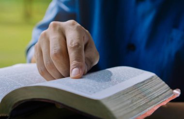 Close up hand of young prayer sitting outdoor for reading bible and worship god, garden nature background. Bible concept.