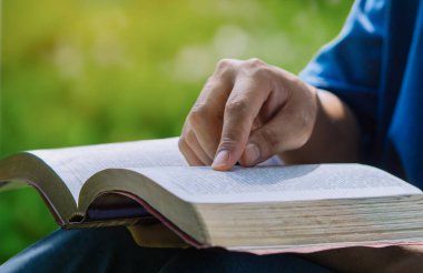 Close up hand of young prayer sitting outdoor for reading bible and worship god, garden nature background. Bible concept.
