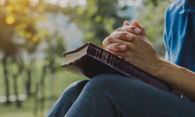 Young prayer sitting outdoor for reading bible and worship god, garden nature background. Bible concept.