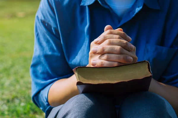 Young prayer sitting outdoor for reading bible and worship god, garden nature background. Bible concept.