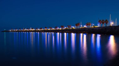 Night of lights reflected in the sea along the tourist port of San Maurizio, Imperia, with the green light of the lighthouse in the background.