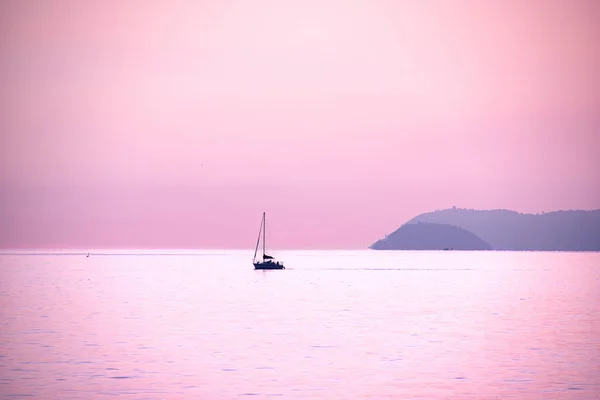 Sailboat silhouette in the Ligurian sea during a stunning autumn sunset that colors both the sky and the sea pink