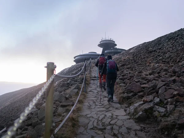 İki erkek turist, dağlık alanda sırt çantalarıyla turistik patika boyunca yürüyorlar.