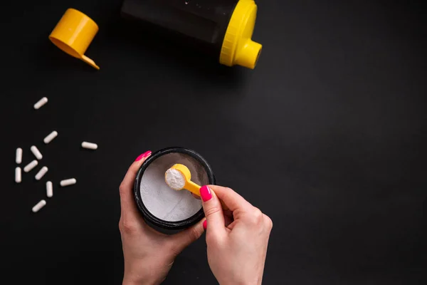 Kreatin. Siyah bir arka planda bir kadının eli spor besininin bir kısmını tutuyor..