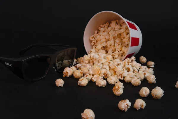 Kırmızı ve beyaz, dağınık bir kova karamelli patlamış mısır ve siyah arka plan manzaralı 3 boyutlu filmler için gözlük. Pankart ya da sinema reklamı konsepti. Metin için yer