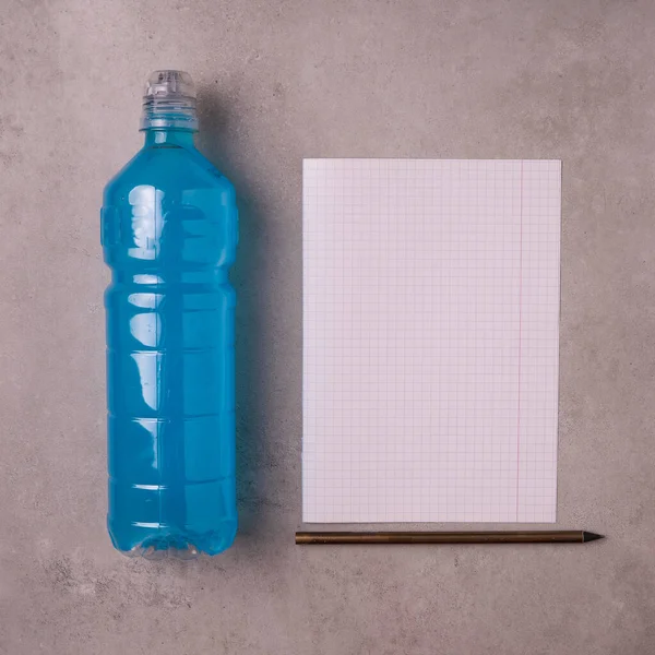 blue isotonic to replenish electrolytes and energy in a plastic bottle on a concrete background piece next to a of blank white paper