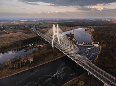 a large white suspension bridge over the river on which cars drive in Wroclaw, Poland, shot from a drone