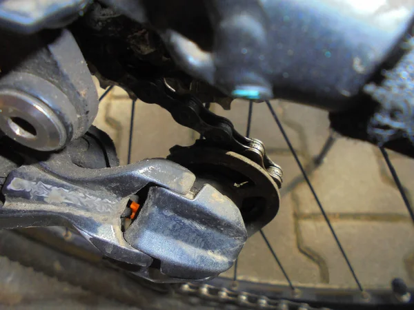 Top gear of mountain bike derailleur covered by dust and dirt hidden in shadows under the bike frame.