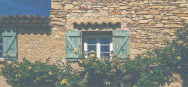 Stone house with windows on summer day with plants. Beautiful traditional old house in French small village. Gordes, Vaucluse, Provence, France. Vintage tone filter effect with noise and grain.