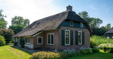 Peaceful rural landscape of Giethoorn village, the Netherlands. House with beautiful flowers in small typical village. Landscape view of houses with canals and rustic thatched roof houses.