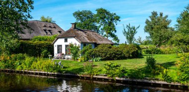 Peaceful rural landscape of Giethoorn village, the Netherlands. House with beautiful flowers in small typical village. Landscape view of houses with canals and rustic thatched roof houses.