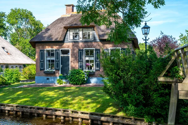 Peaceful rural landscape of Giethoorn village, the Netherlands. House with beautiful flowers in small typical village. Landscape view of houses with canals and rustic thatched roof houses.