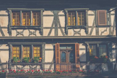 Pencereleri ve koyu keresteleri olan eski bir ev duvarı. Tarihi şehir Colmar, Fransa, Alsace 'de geleneksel ahşap panjurları ve çiçekleri olan geleneksel ahşap evlerin önü..