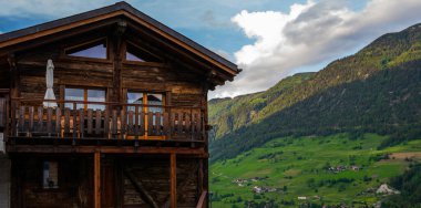 Baharda mavi gökyüzü olan güneşli bir günde İsviçre Alp köyündeki tipik ahşap evden dağlardaki yeşil çayır manzarası.