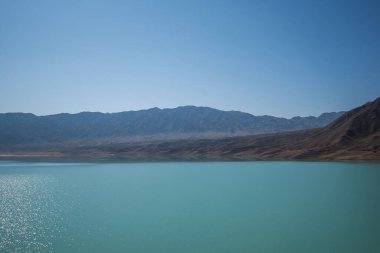 Arka planda dağlar olan göl. Dağ manzaralı. Çöl dağları üzerinde bunaltıcı bir sis ve tuzlu bir turkuaz göl..