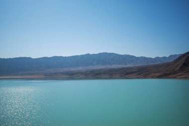 Arka planda dağlar olan göl. Dağ manzaralı. Çöl dağları üzerinde bunaltıcı bir sis ve tuzlu bir turkuaz göl..