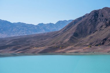 Uzakta mavi sisli dağları olan cansız bir vadinin ortasında turkuaz bir göl. Parlak gölü olan gri, donuk dağlar..
