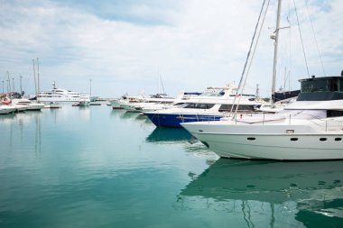 Lüks yatlar limana yanaştı. Modern motorlu teknelerin ve gök mavisi suyun deniz parkı. Huzur, rahatlama ve şık bir tatil. Limanda demirlemiş beyaz yatlar ve yelkenliler, yaz mevsimi..