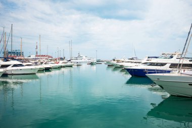 Lüks yatlar limana yanaştı. Modern motorlu teknelerin ve gök mavisi suyun deniz parkı. Huzur, rahatlama ve şık bir tatil. Limanda demirlemiş beyaz yatlar ve yelkenliler, yaz mevsimi..