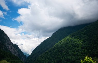 Dağlarda ve bulutlarda bahar sabahı. Ağaçlı atmosferik manzara ve bulutlu gökyüzünde alçak bulutlar. Muhteşem dağ manzarası..