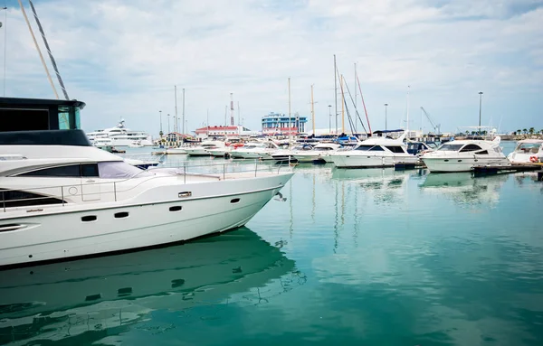 Lüks yatlar limana yanaştı. Modern motorlu teknelerin ve gök mavisi suyun deniz parkı. Huzur, rahatlama ve şık bir tatil. Limanda demirlemiş beyaz yatlar ve yelkenliler, yaz mevsimi..