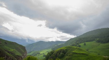Kafkasya Dağları 'ndaki güzel bahar manzarası yemyeşil tepeler ve kayalık yamaçlar. Yağmurlu bir günde dramatik bulutlu gökyüzü. Dağların tepesinde alçak bulutlar.