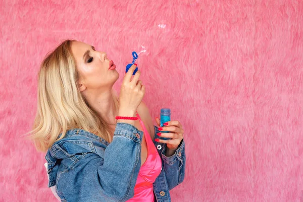 Güzel kaygısız kadın pembe arka planda sabun köpükleri tutuyor. Reklam bilgileriniz için boş yer var..