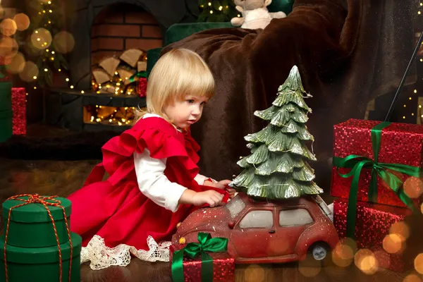 Mutlu Noeller ve mutlu tatiller! Kırmızı elbiseli şirin bir çocuk şöminenin yanında oyuncaklarla oynuyor. Yeni yıl ve Noel konsepti