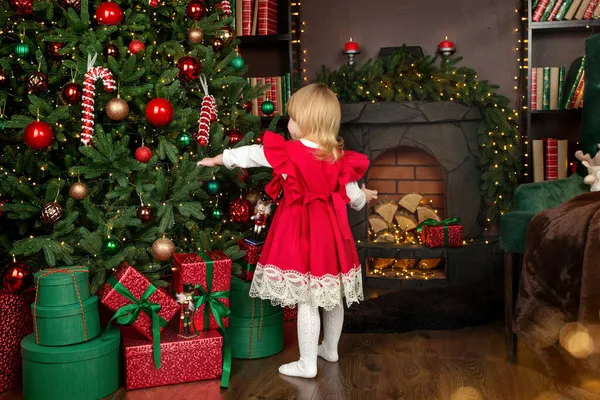 Noel ve yeni yıl beklentisiyle, mutlu küçük bir kız Noel ağacındaki oyuncakları inceliyor. Mutlu Noeller ve mutlu yıllar konsepti