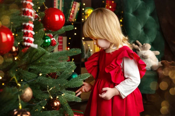 Noel ve yeni yıl beklentisiyle, mutlu küçük bir kız Noel ağacındaki oyuncakları inceliyor. Mutlu Noeller ve mutlu yıllar konsepti