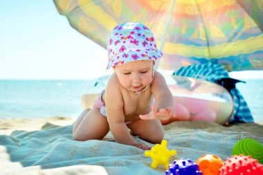 Bebek plajda oynuyor. Denizde bir çocuk. Kum ve su için oyuncaklar. Küçük çocuklar için güneş koruması.