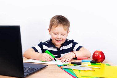Okula dönelim. Küçük mutlu öğrenci masada resim çiziyor. Çocuk ödevini tablet bilgisayarla yapıyor..