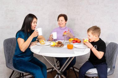 Büyükanne, anne ve çocuk. Mutlu çok nesilli aile yemek masasında toplanıyor ve öğle yemeğinde eğleniyor.