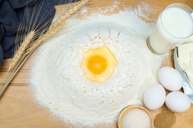 Ahşap bir masada yumurta, un, şeker, maya pişirmek için gerekli malzemeler.