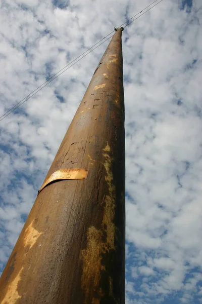 A large old telephone pole stretches up into a cloudy sky — Stock Photo, Image