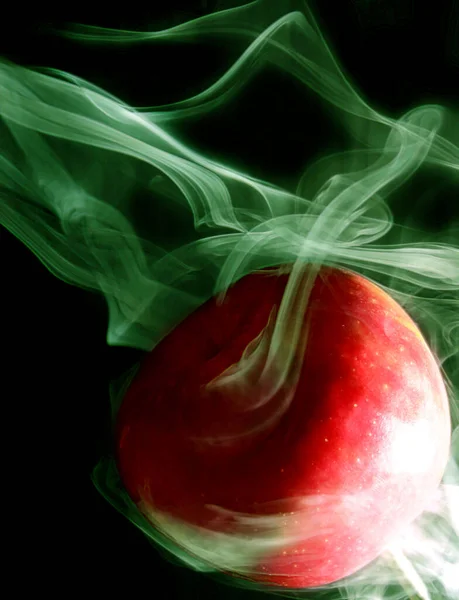 Зеленый дым окружает круглое красное яблоко на черном фоне — стоковое фото