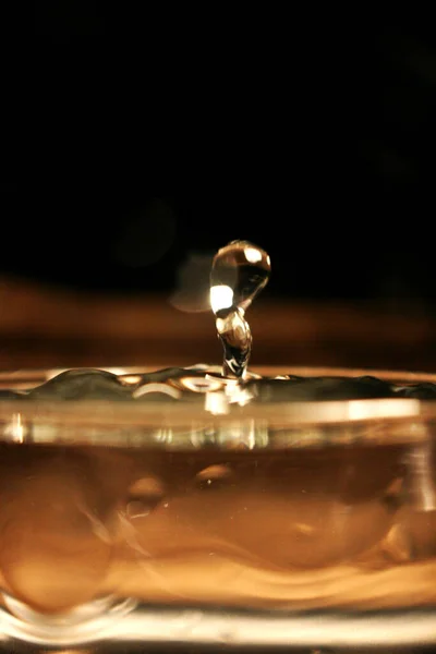 Wasser plätschert in einem Glas auf braunem Bernstein-Hintergrund — Stockfoto