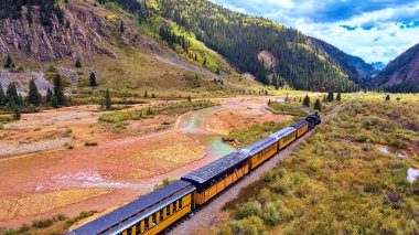 Sonbaharda nehir ve dağların yanındaki vadiden geçen tren.