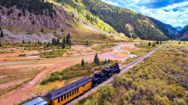 Kömürlü klasik tren nehir boyunca dağlardaki vadi boyunca yolcuları sürüklüyor.