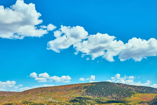 Голубое небо с небольшими облаками на фоне разноцветного холма — стоковое фото
