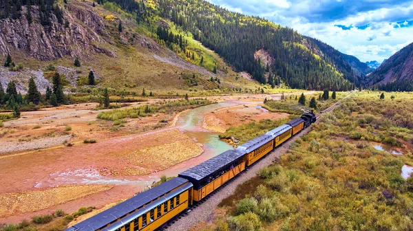 Sonbaharda nehir ve dağların yanındaki vadiden geçen tren.