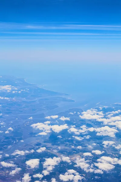 Airplane view of clouds and blue sky with land in distance — Stock Photo, Image